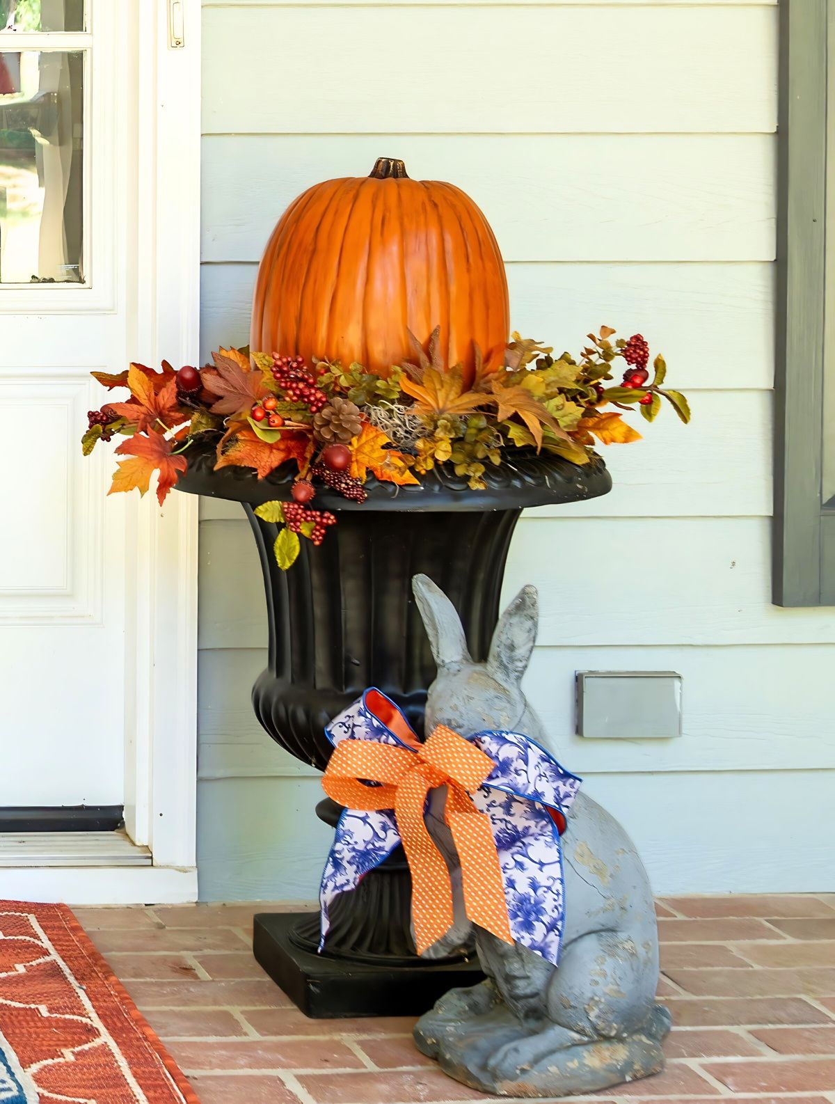 fall arrangement with a large pumpkin and floral picks in a tall black urn on a front porch