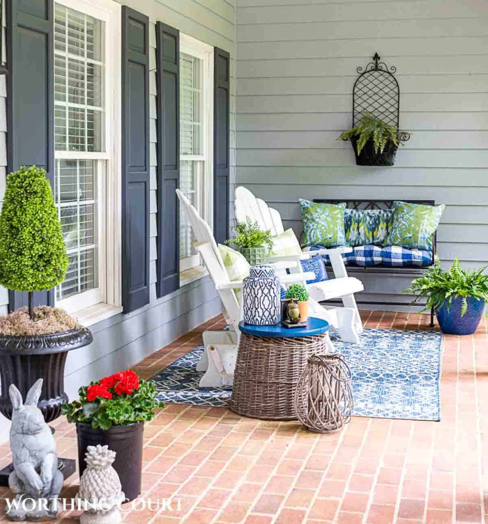 view of one end of a long front porch with white gliders and blue and white accessories decorated for summer