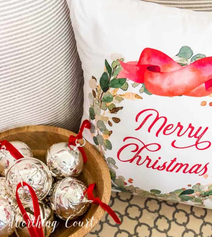 silver bells in a wooden bowl beside a Merry Christmas pillow