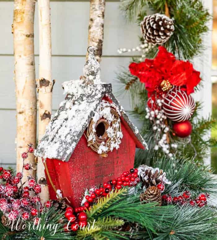 red birdhouse in a bed of Christmas greens in a planter