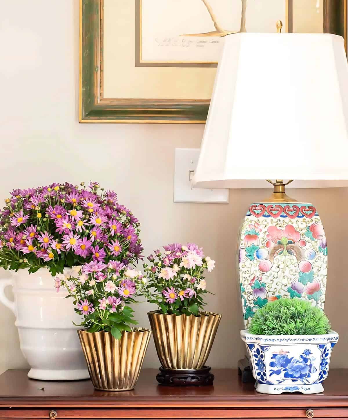 three purple mums in various containers on a wooden chest