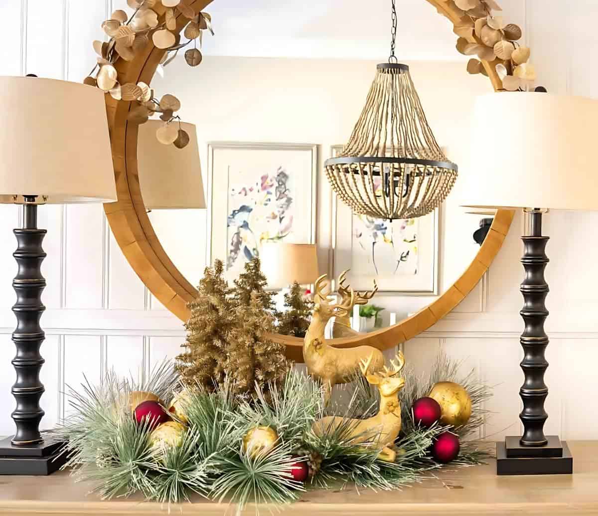 Christmas vignette on a sideboard with gold deer and gold tinsel trees in front of a round mirror