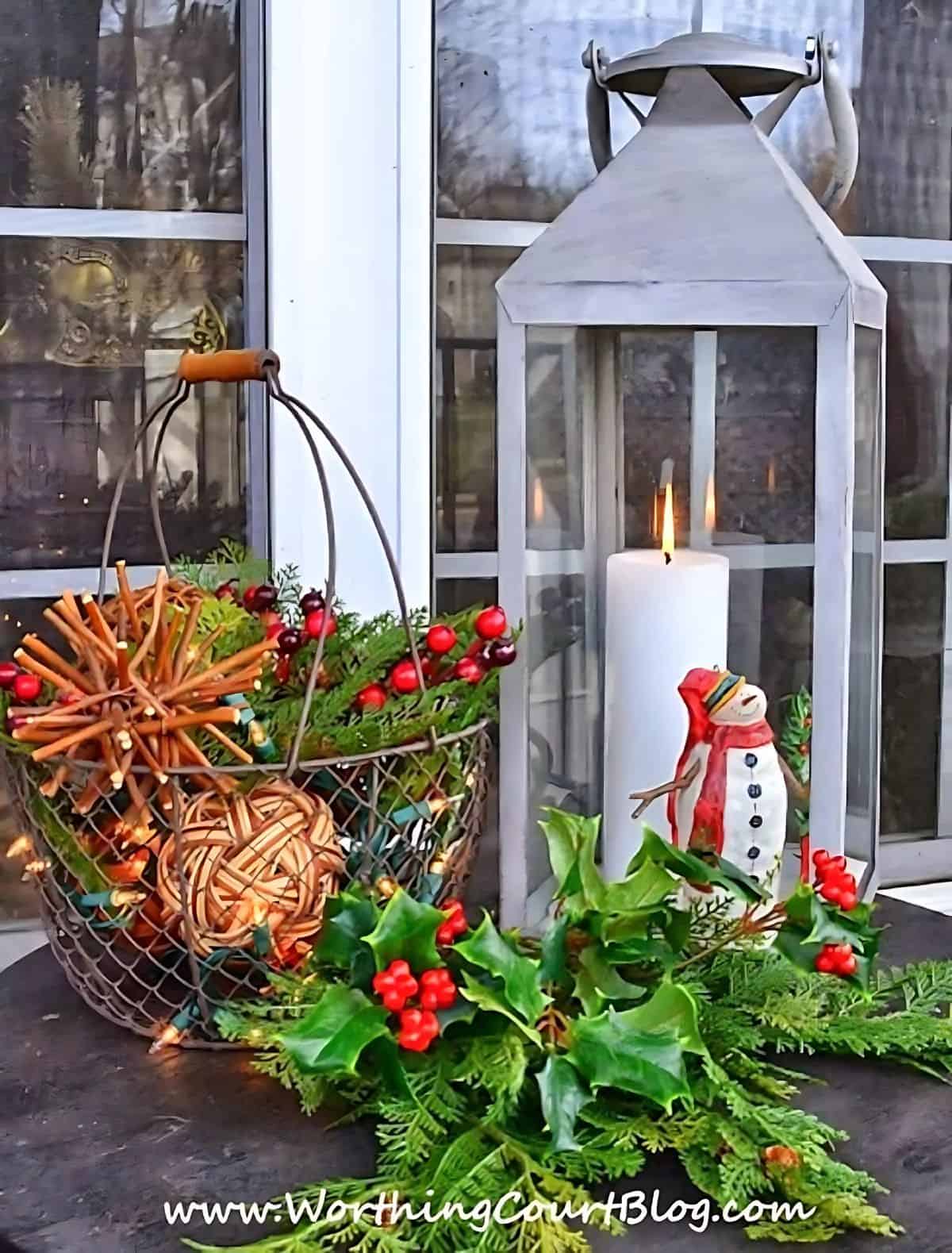 Christmas vignette on an outdoor table with a lantern and basket filled with greenery and grapevine orbs