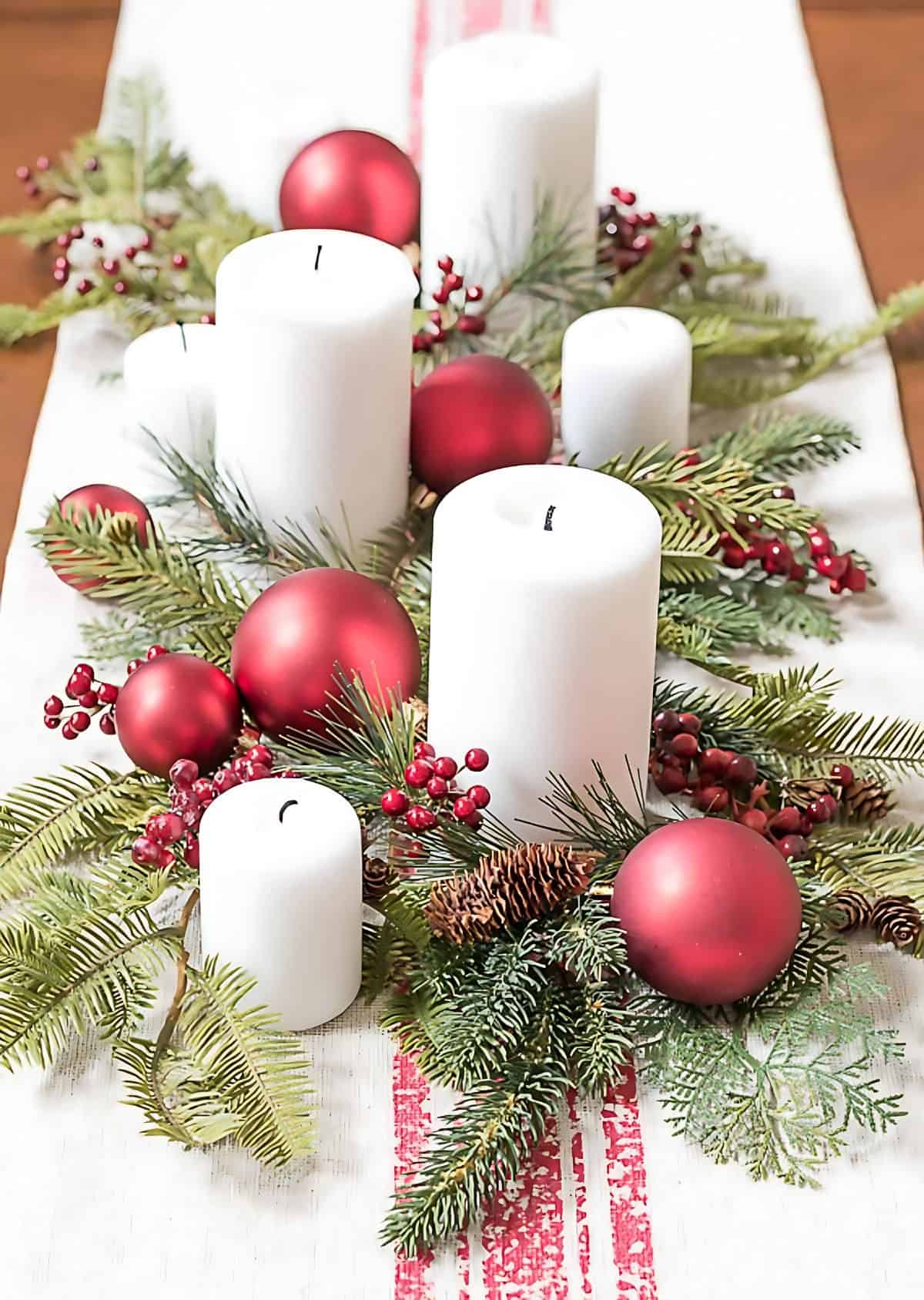 white pillar candles mixed with Christmas greenery and red ornaments on a coffee table