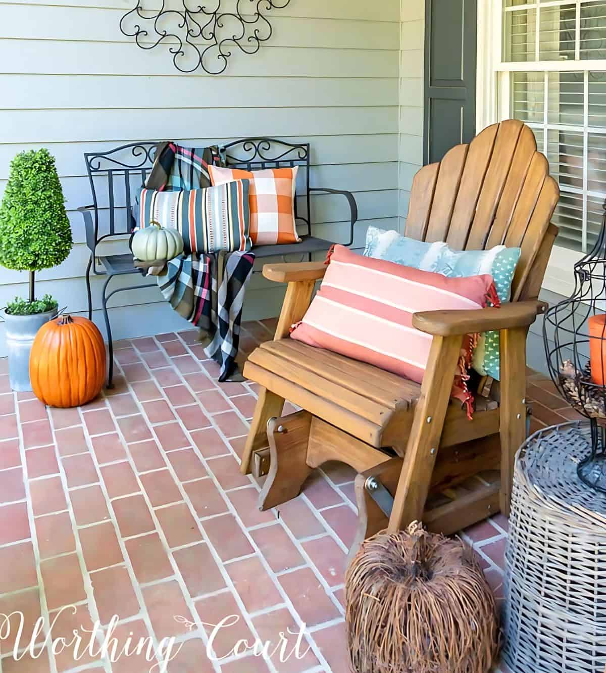 wood adirondack glider and black metal bench on a front porch with fall pillows