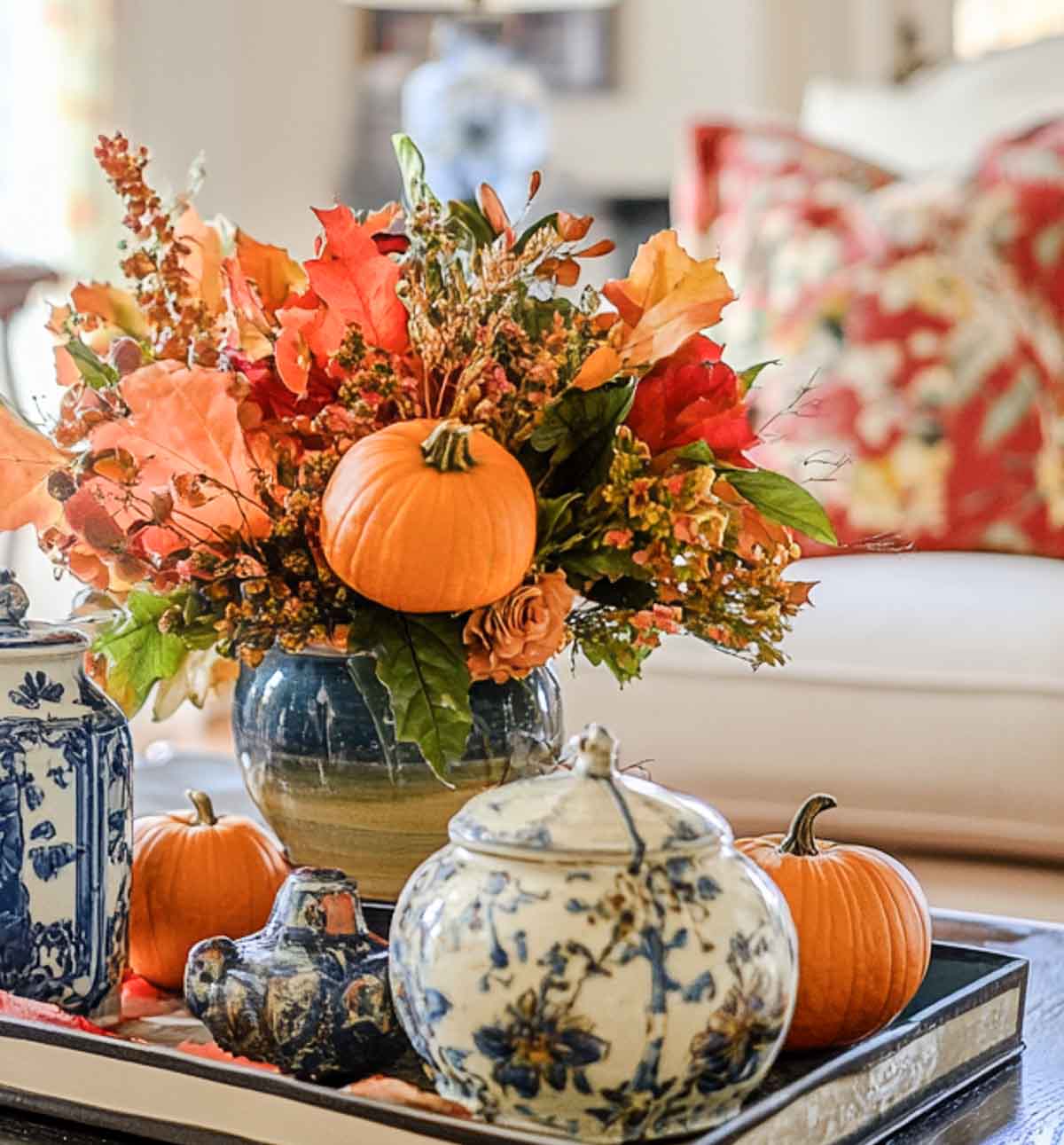 vase filled with fall foliage in a tray with blue and white accessories on a coffee table