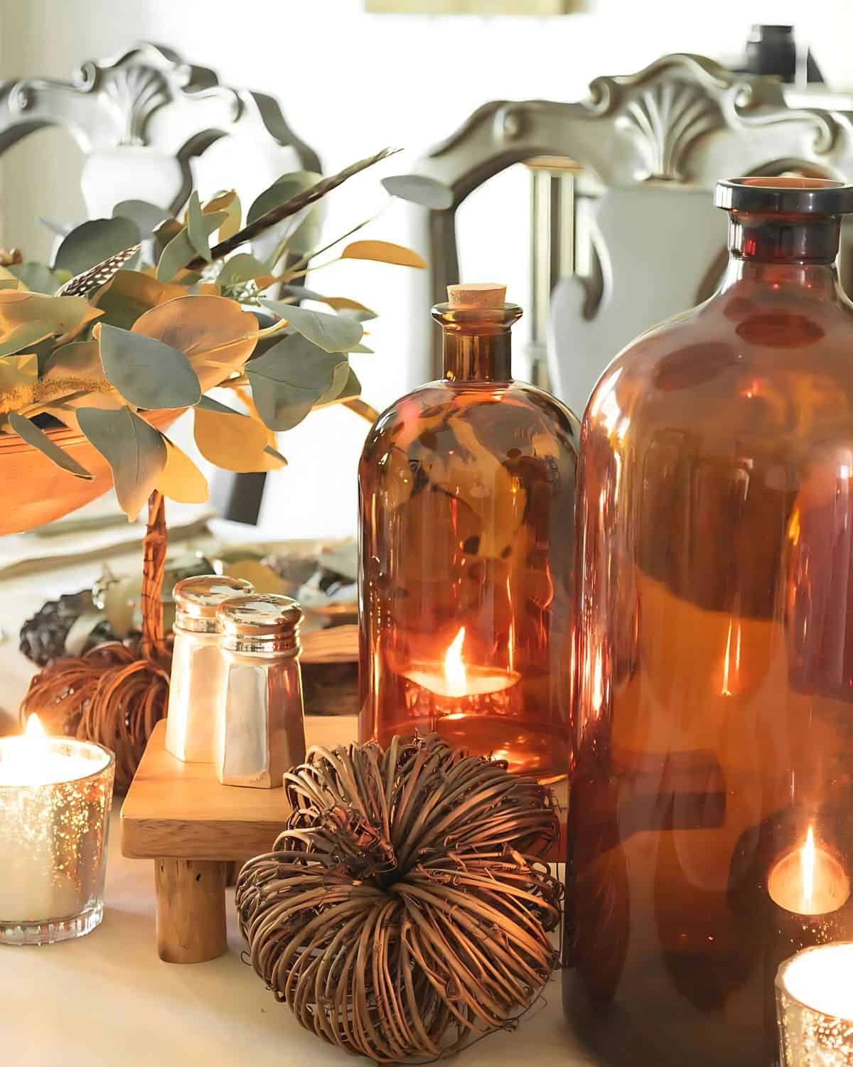 Thanksgiving centerpiece with large amber bottles, wicker pumpkins, and mercury glass candle holders