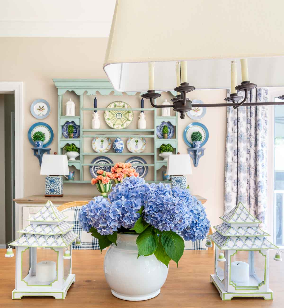 centerpiece on a table with blue hydrangeas and white and blue pagoda shaped lanterns with a plate rack in the background