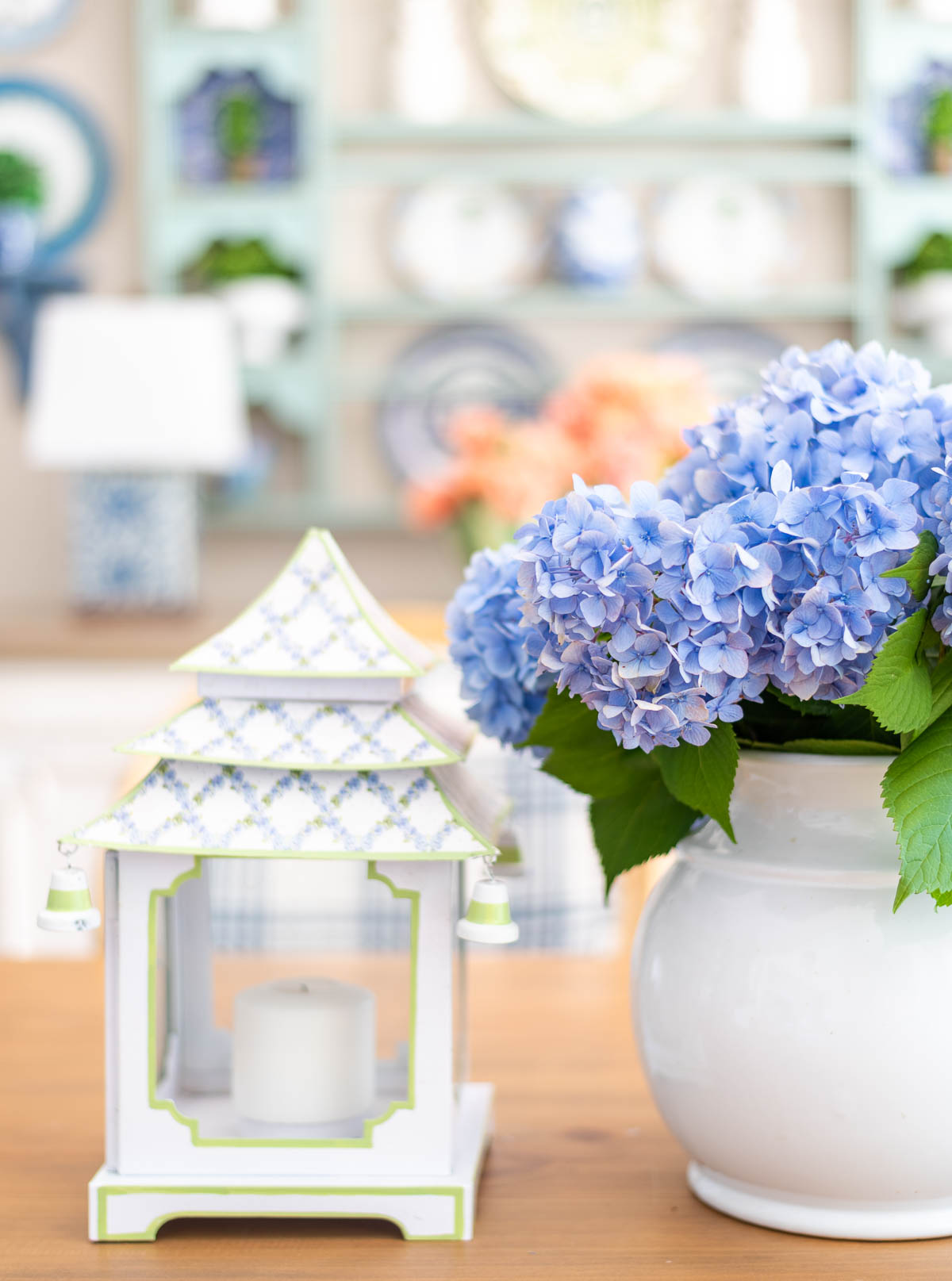 centerpiece on a table with blue hydrangeas and white and blue pagoda shaped lanterns with a plate rack in the background