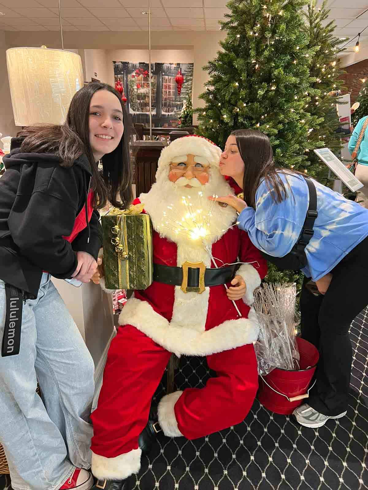 2 girls pretending to kiss a Santa figurine