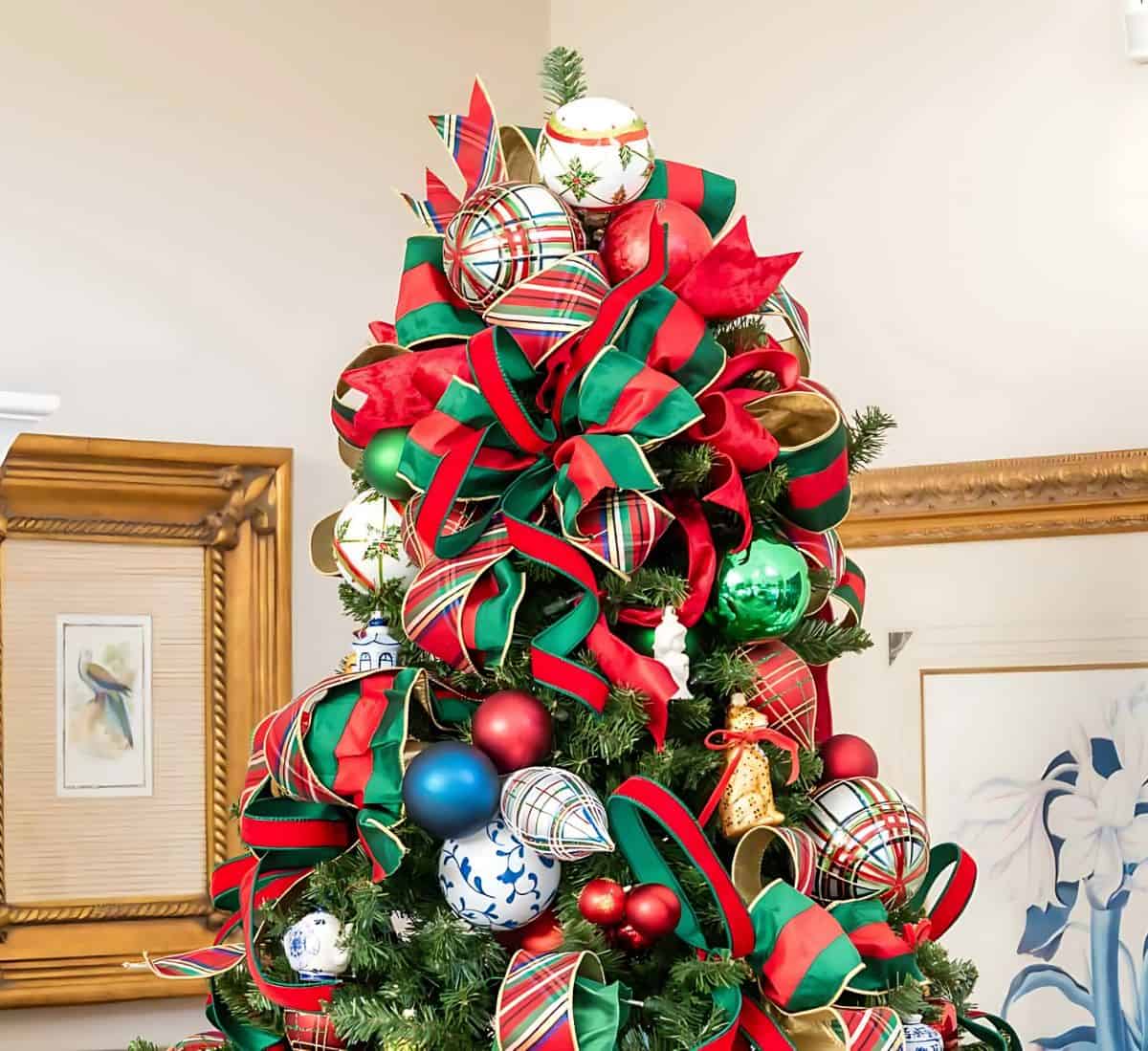 top of Christmas tree decorated with red and green ornaments and plaid ribbon